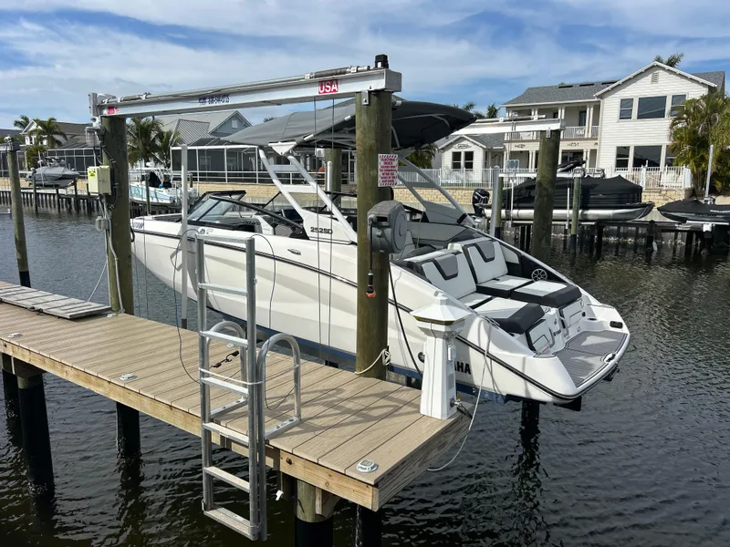 Slide: The Image of 2023 Yamaha Boats 252SD on dock lift, waterfront homes in background. - 2