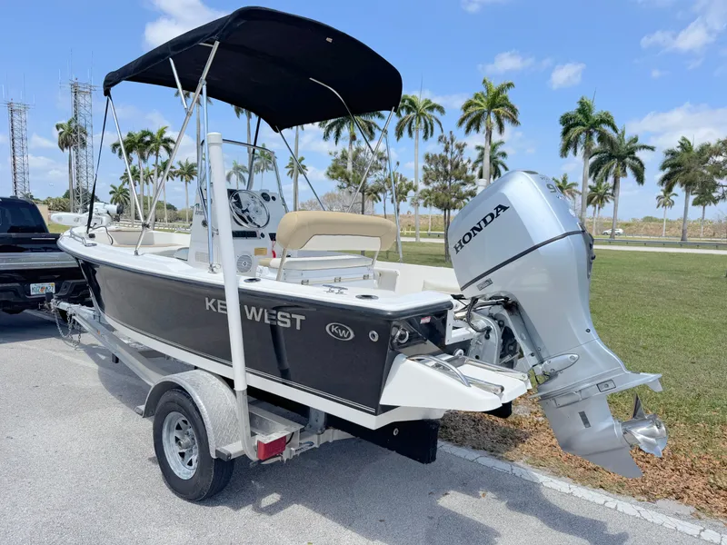 Slide: The Image of 2016 Key West 1720 Center Console boat with Honda outboard motor on trailer, parked near palm trees. - 2