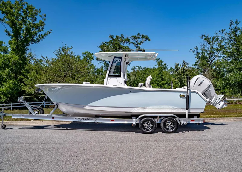 Slide: The Image of 2025 Sea Hunt Ultra 245 SE boat on trailer, parked on road with trees in background. - 5