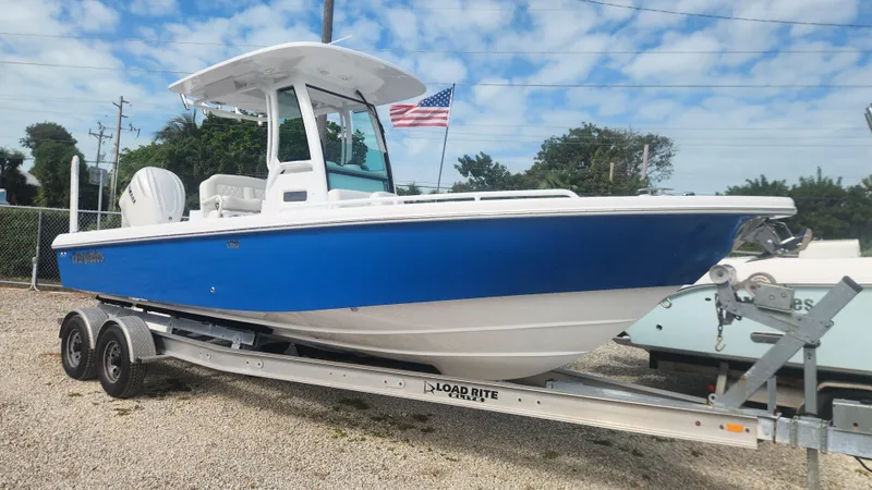 The Image of 2025 Everglades 253 Center Console boat on trailer, blue hull, American flag in background. - 0