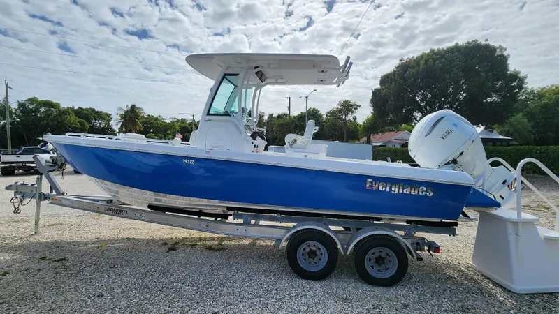 Slide: The Image of 2025 Everglades 253 Center Console boat on trailer, blue hull, parked outdoors. - 2