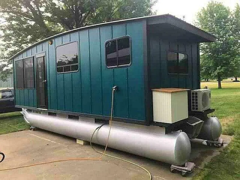 Slide: The Image of Custom 2023 houseboat with teal exterior on pontoons, parked on concrete. - 29