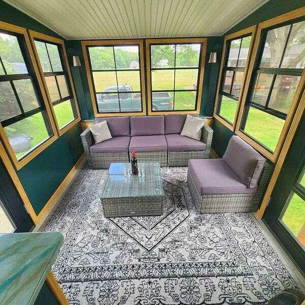 Slide: The Image of Cozy sunroom with wicker furniture, patterned rug, and large windows overlooking a green landscape. - 9