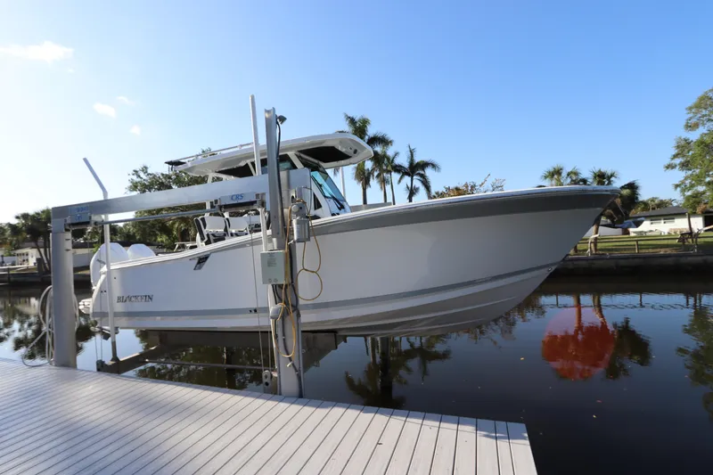 Slide: The Image of 2023 Blackfin 272 CC boat docked on a lift by a calm waterfront. - 0