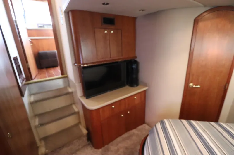 Slide: The Image of 2000 Cruisers Yachts 4450 Express Motoryacht interior with TV, wooden cabinetry, and striped bedding. - 46