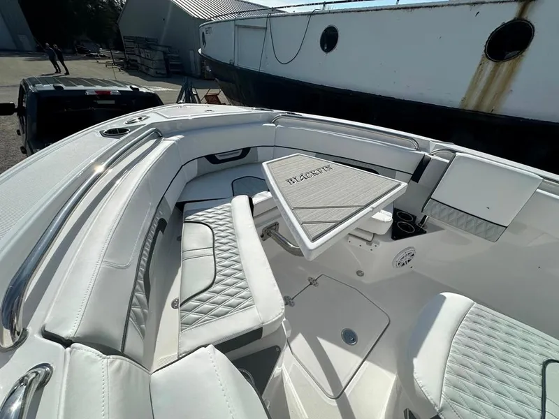 Slide: The Image of 2024 Blackfin 222CC boat interior with white seating and table, docked near a large vessel. - 31