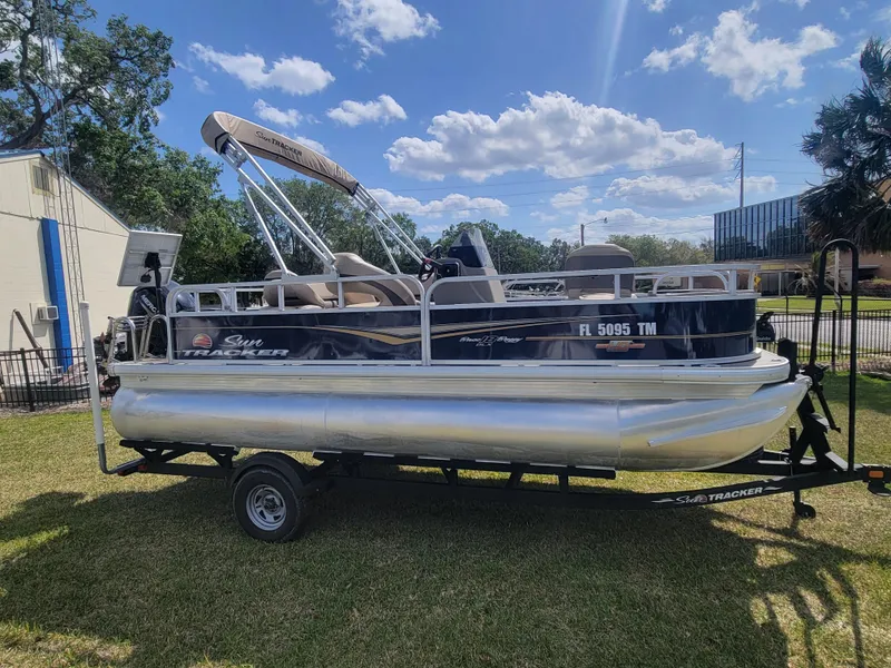 Slide: The Image of 2023 Sun Tracker Bass Buggy 18 DLX pontoon boat on trailer, parked on grass. - 2