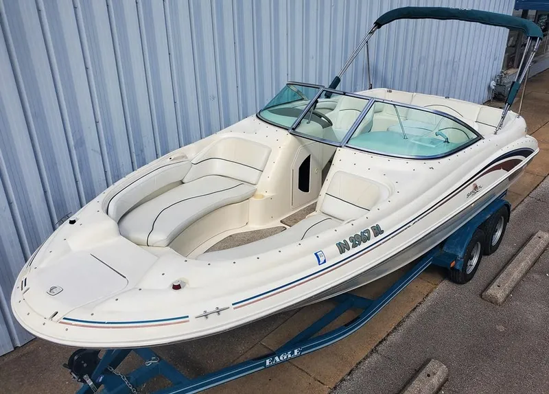 Slide: The Image of 1998 Sea Ray 210 Sundeck boat on trailer, white exterior, blue accents, parked by a metal wall. - 1