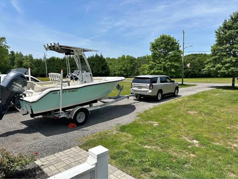 Slide: The Image of 2023 Key West 203 FS boat on trailer, hitched to an SUV in a sunny driveway. - 3