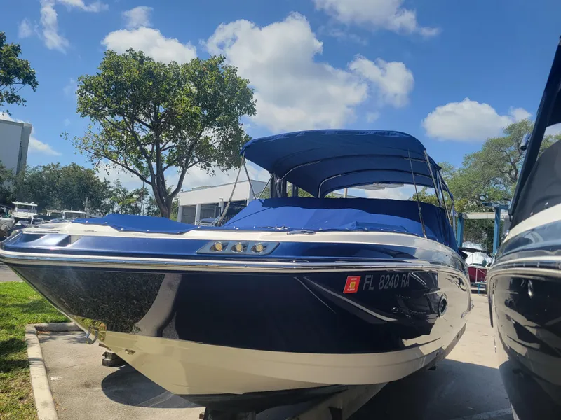 Slide: The Image of 2015 Chaparral 250 Suncoast boat with blue canopy, parked outdoors under a sunny sky. - 1