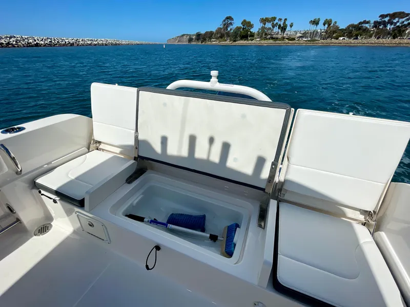 Slide: The Image of 2022 Robalo R230 Center Console boat interior with storage compartment, docked by scenic coastline. - 16