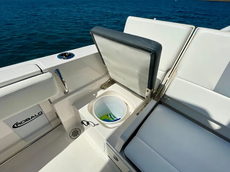 Slide: The Image of 2022 Robalo R230 Center Console boat with open storage compartment, white seating, and ocean backdrop. - 17