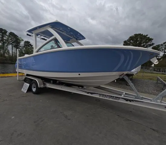 Slide: The Image of 2025 Robalo 257 Dual Console boat on trailer, blue and white design, parked outdoors. - 2