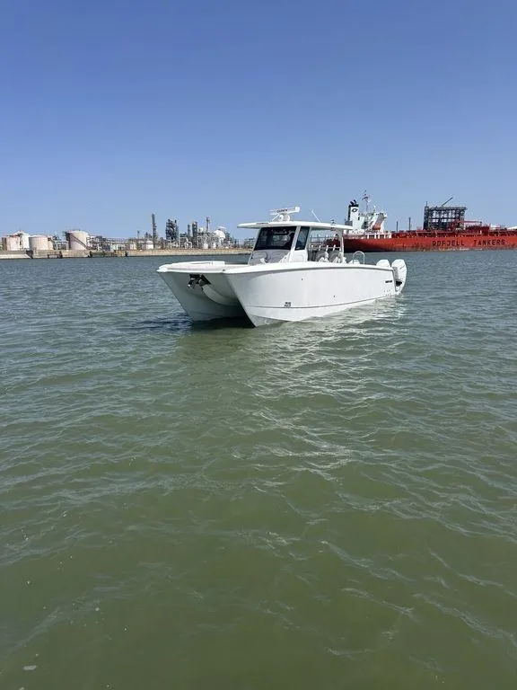 Slide: The Image of 2024 Twin Vee 400 GFX boat on calm water with industrial background. - 3
