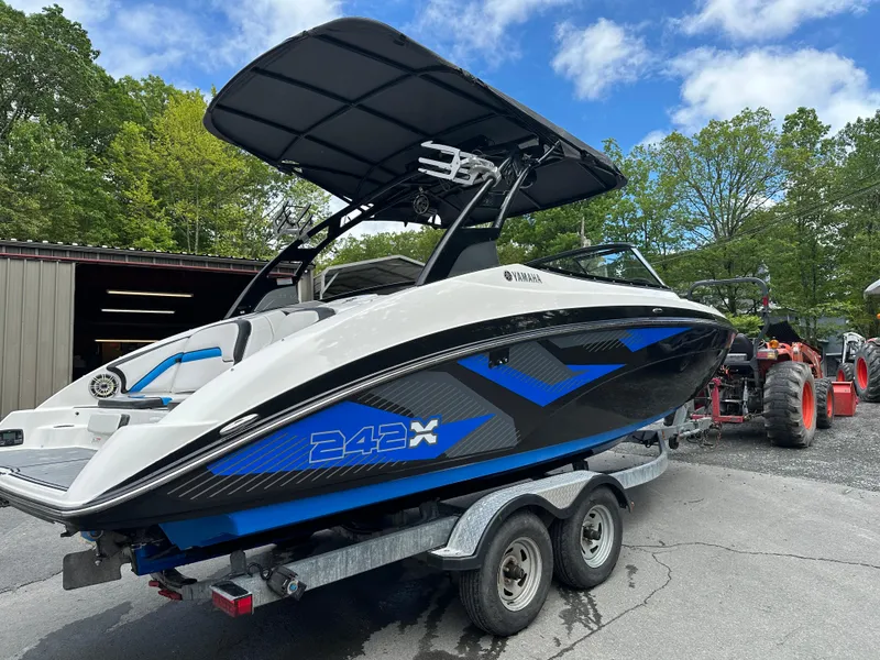 Slide: The Image of 2016 Yamaha Boats 242X E-Series on trailer, parked outdoors near trees and a building. - 13