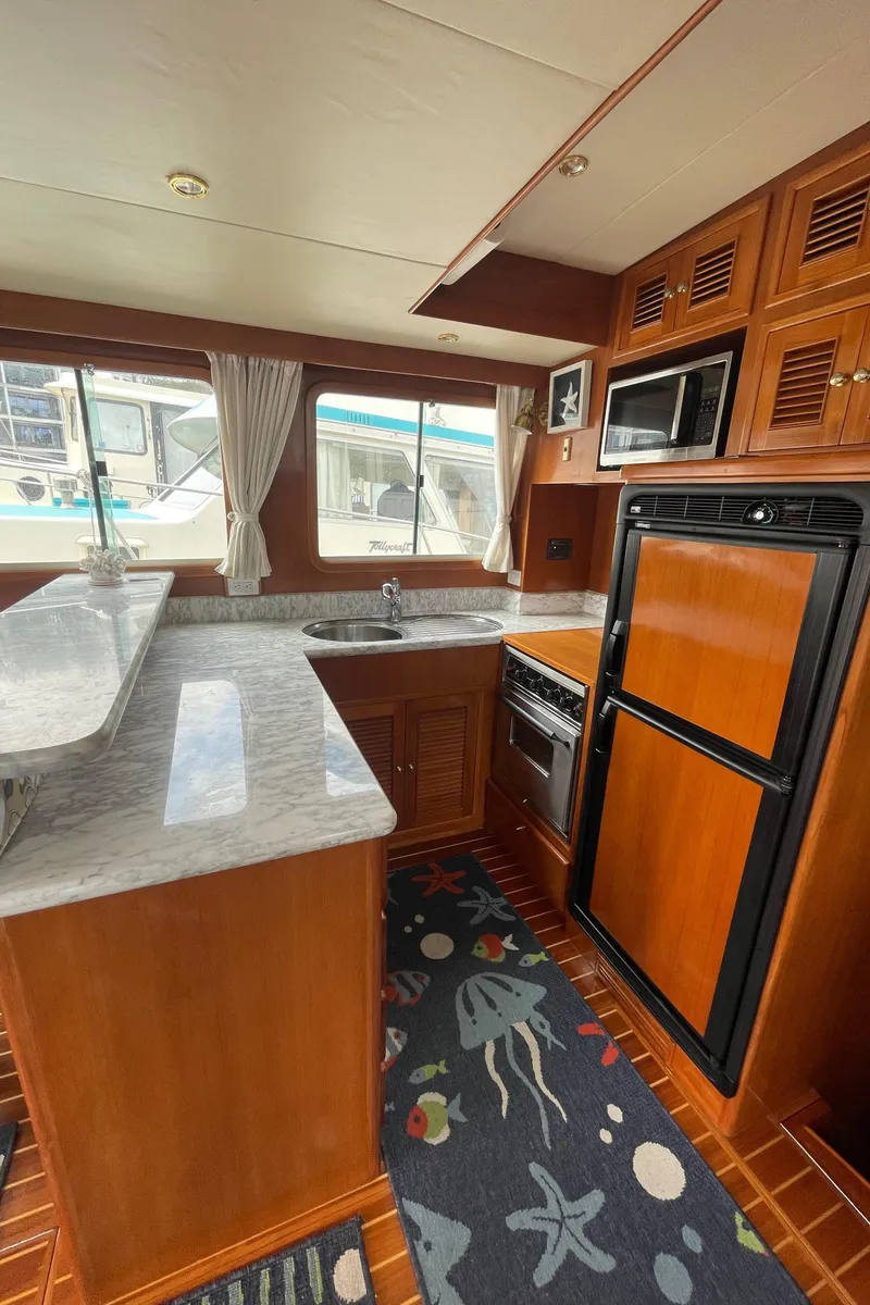 Slide: The Image of 2006 North Pacific 42 yacht kitchen with wood cabinetry, marble countertops, and nautical-themed rug. - 10