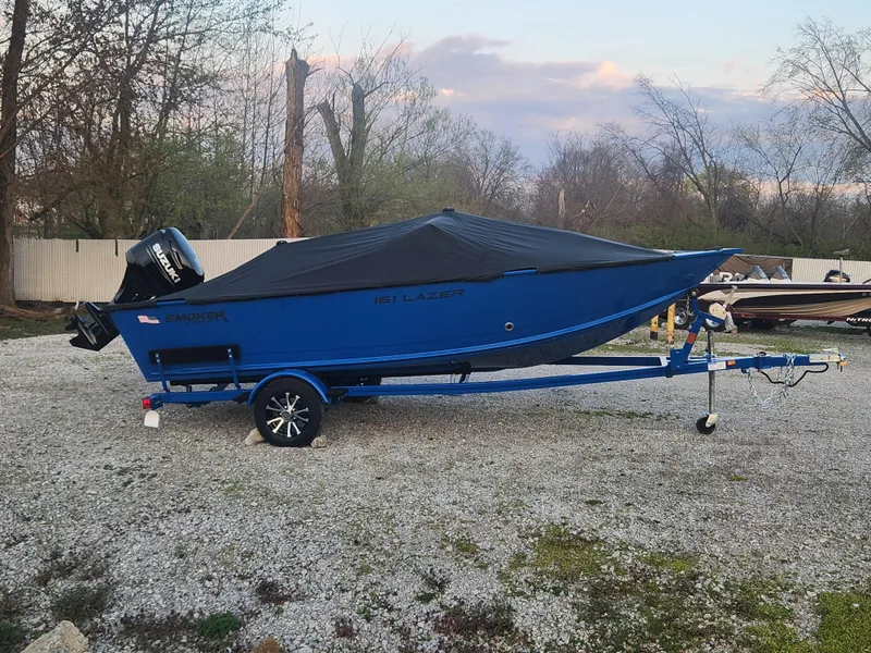 Slide: The Image of 2025 Smoker Craft Lazer 161 boat on trailer, covered, parked on gravel. - 18