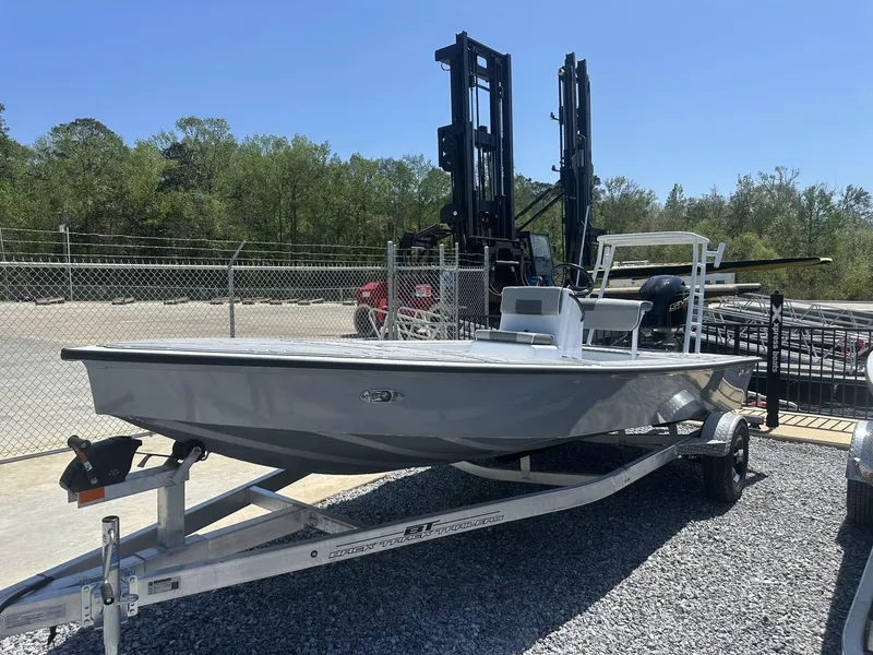 Slide: The Image of 2025 Xpress Skiff 185 boat on trailer, parked outdoors near trees and industrial equipment. - 5