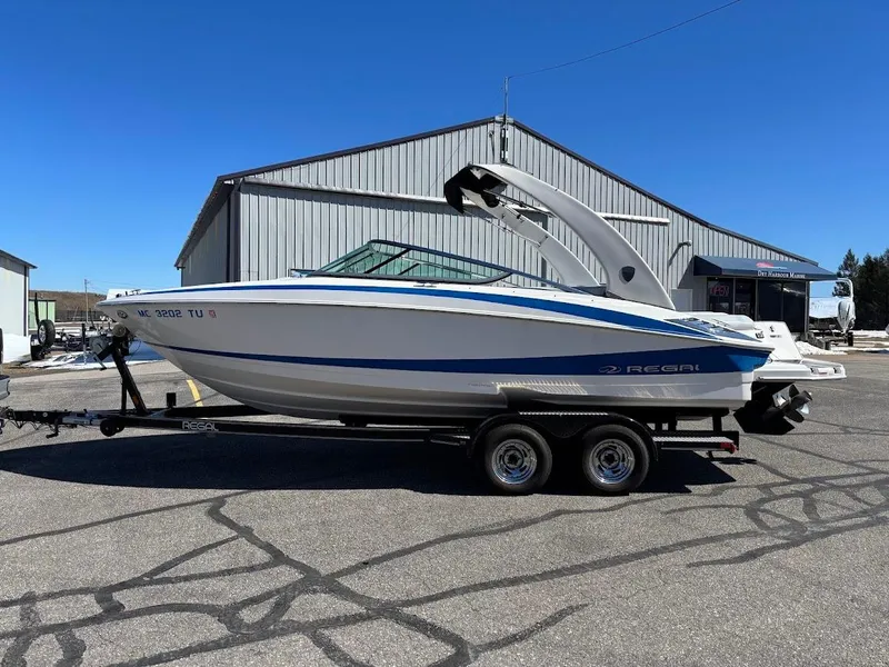 Slide: The Image of 2013 Regal 2300 Bowrider boat on trailer, parked outside a large warehouse. - 1