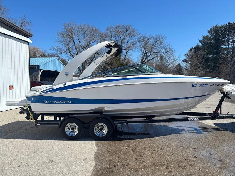 Slide: The Image of 2013 Regal 2300 Bowrider boat on trailer, white with blue accents, parked outdoors. - 2