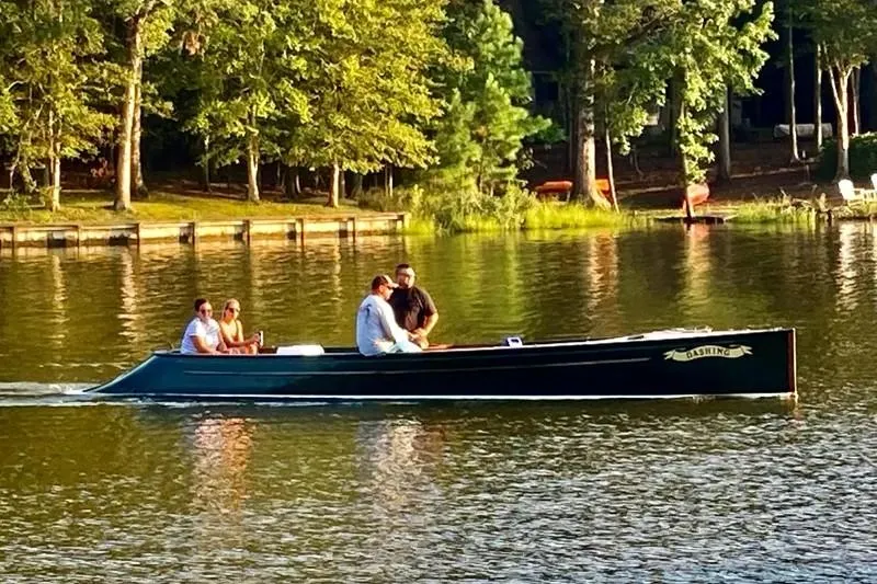 Slide: The Image of Classic English Launch boat from 1990 on a serene lake with passengers, surrounded by trees. - 1