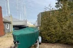 Slide: The Image of 1990 Classic English Launch boat covered, parked outdoors near buildings and trees. - 49
