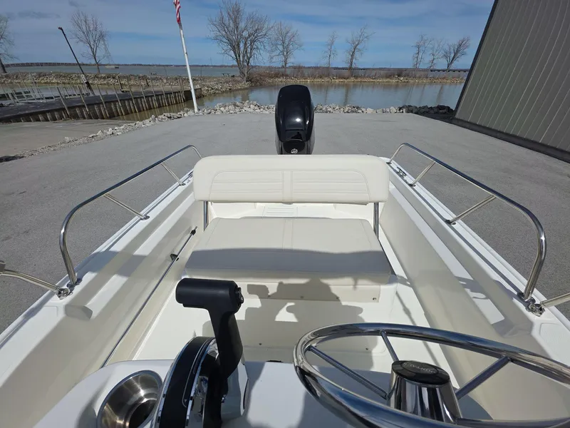 Slide: The Image of 2024 Boston Whaler 150 Montauk boat interior with steering wheel and seating, dockside view. - 10