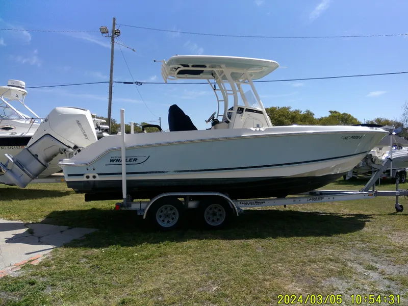 Slide: The Image of 2021 Boston Whaler Outrage 230 boat on trailer, parked outdoors under clear sky. - 6