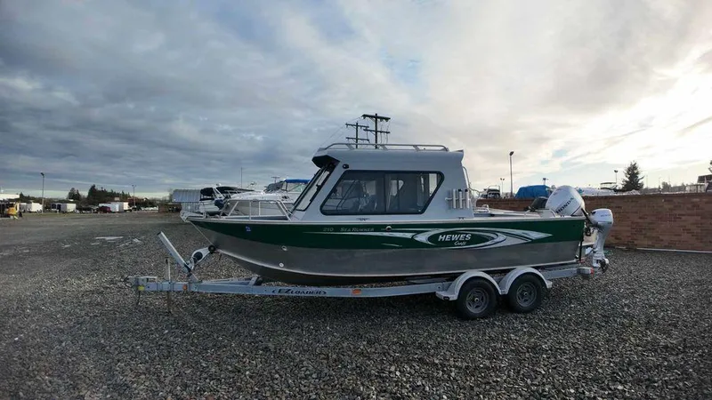 Slide: The Image of 2018 Hewescraft 210 Sea Runner boat on trailer, parked outdoors under cloudy sky. - 2