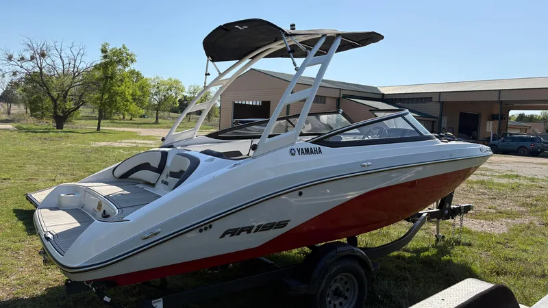 Slide: The Image of 2024 Yamaha Boats AR195, rear view, parked on grass with trailer nearby. - 13