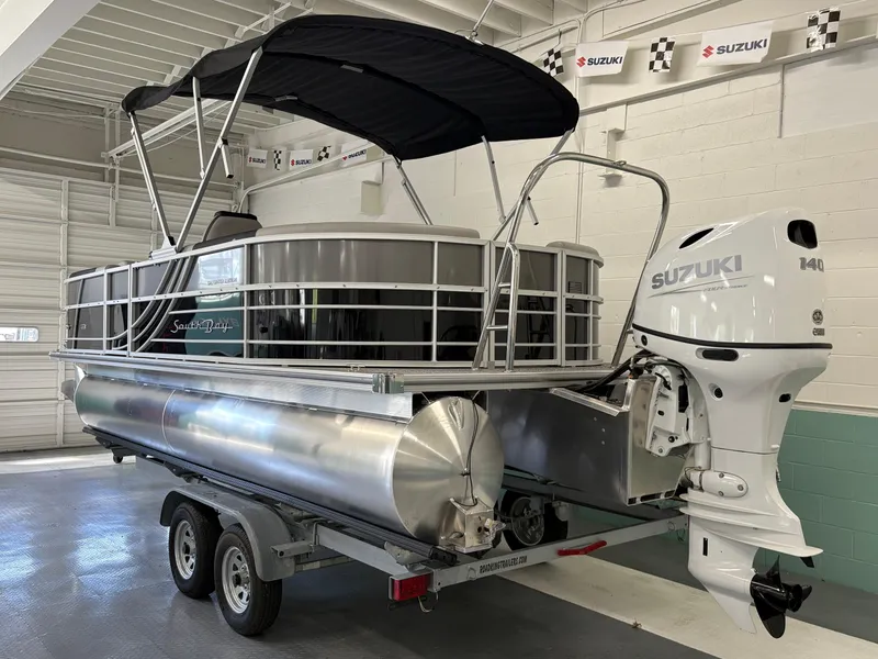 Slide: The Image of 2025 South Bay 222RS pontoon boat with Suzuki 140 outboard motor in a showroom. - 2