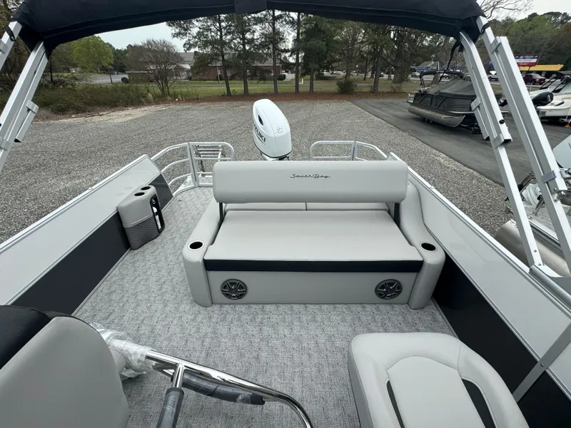 Slide: The Image of 2025 South Bay 224UL pontoon boat interior with seating and motor, parked on gravel. - 13