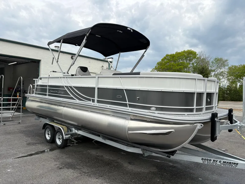 Slide: The Image of 2025 South Bay 224UL pontoon boat on trailer, parked outdoors under cloudy sky. - 4