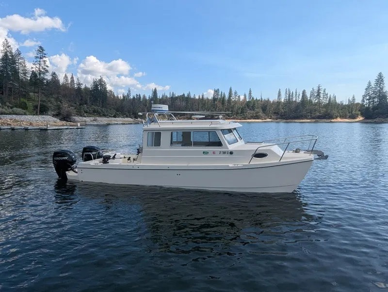 Slide: The Image of 2008 C-Dory 255 TOMCAT boat on calm water, surrounded by trees and blue sky. - 0