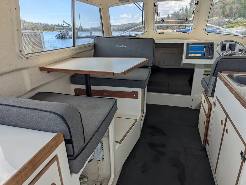 Slide: The Image of 2008 C-Dory 255 TOMCAT interior with seating, table, and navigation equipment, overlooking a scenic waterfront. - 19