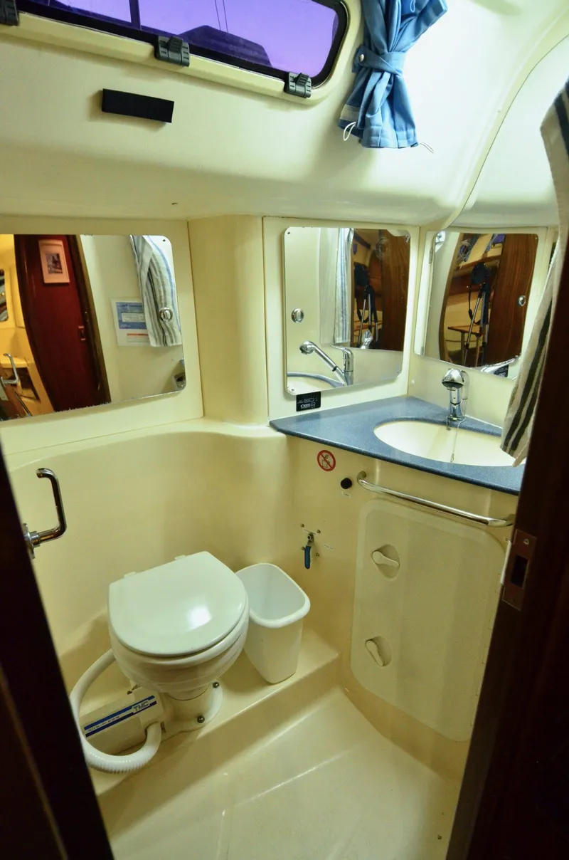 Slide: The Image of 2003 Bavaria 49 yacht bathroom with toilet, sink, mirror, and window. - 22