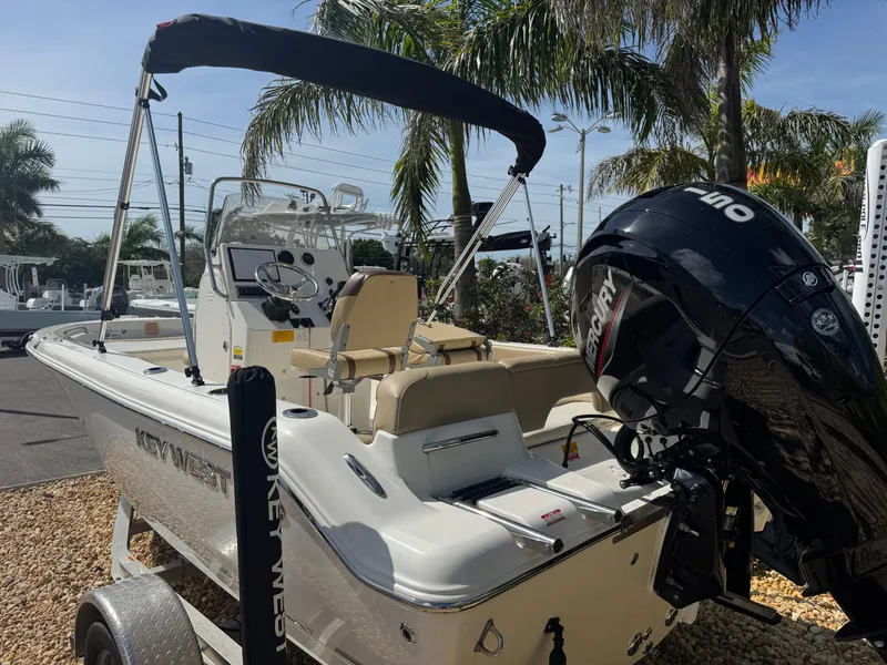 Slide: The Image of 2019 Key West 189 FS boat with outboard motor, parked on a trailer, surrounded by palm trees. - 17