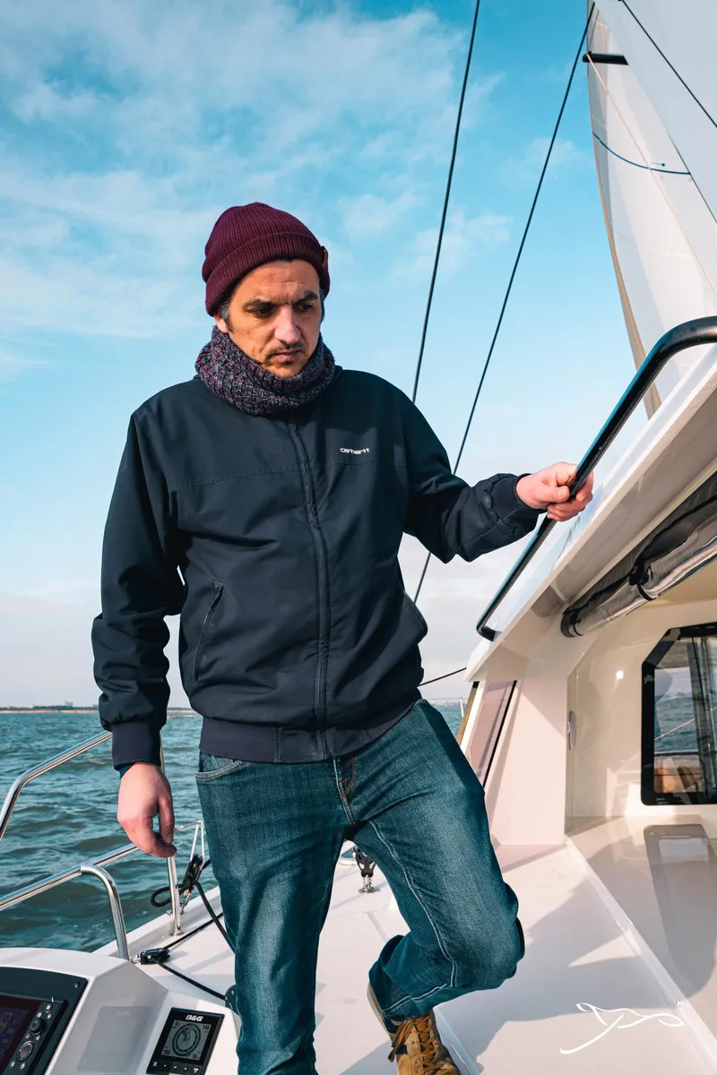 Slide: The Image of Man on Nautitech 40 Open 2025 sailboat, wearing a beanie and jacket, under clear blue sky. - 20