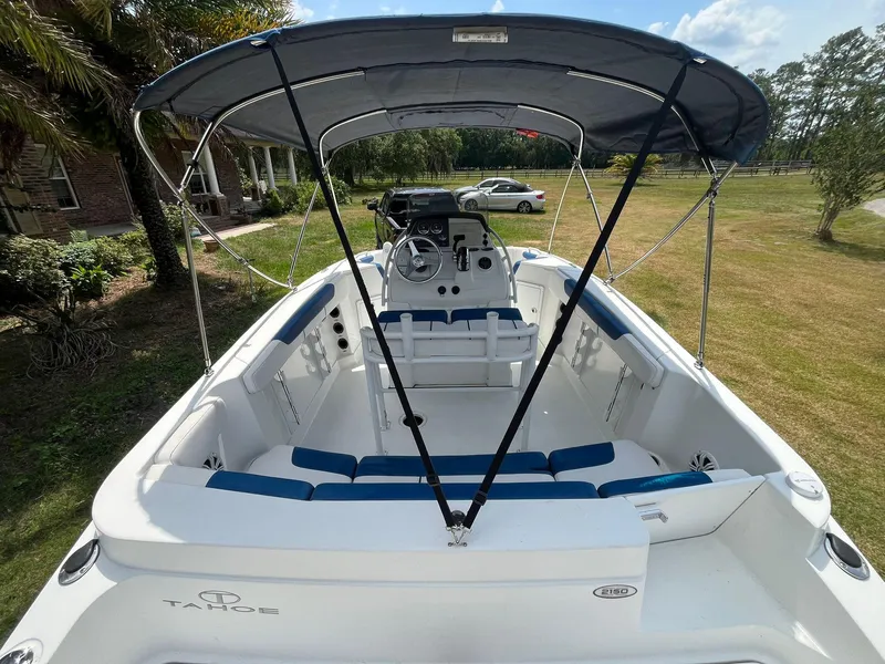 Slide: The Image of 2020 Tahoe 2150 CC boat with canopy, white and blue seating, parked on grass. - 13