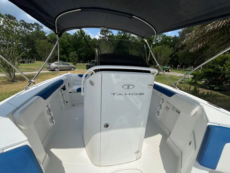 Slide: The Image of 2020 Tahoe 2150 CC boat interior with canopy, white and blue seating, and lush greenery background. - 38