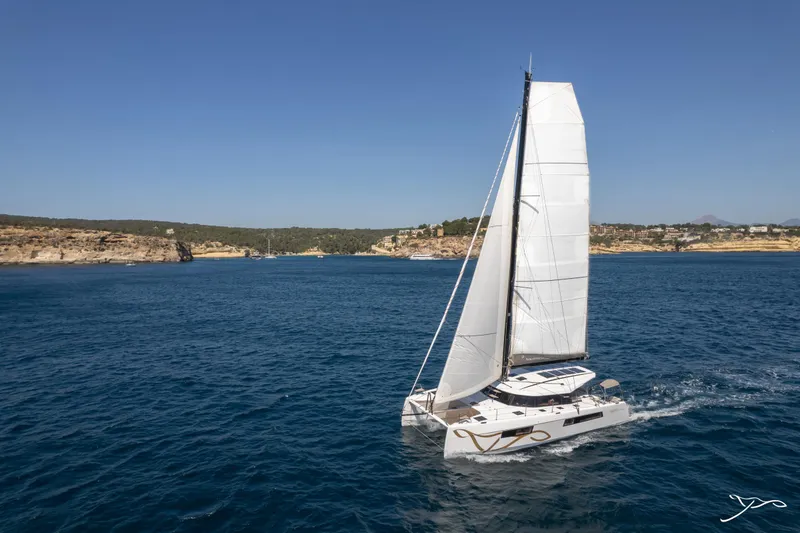 Slide: The Image of Sailing catamaran Nautitech 44 Open 2025 gliding on blue ocean near rocky coastline. - 1