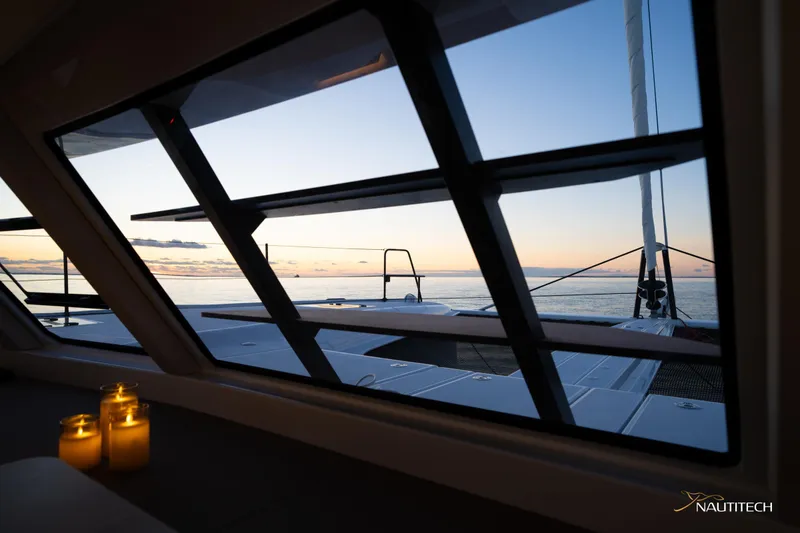 Slide: The Image of 2025 Nautitech 48 Open yacht interior with ocean view at sunset, featuring lit candles. - 46