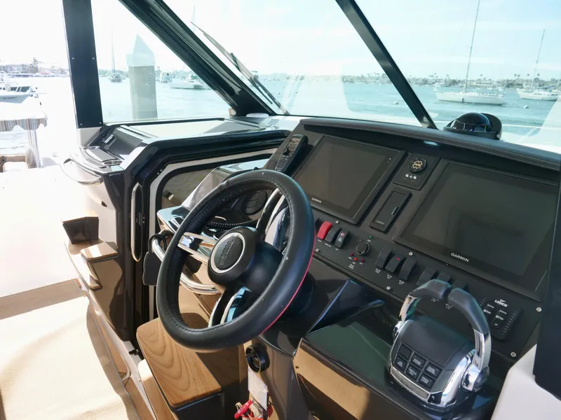 Slide: The Image of 2016 Tiara Yachts Q44 helm with modern controls and navigation screens, docked by the water. - 14