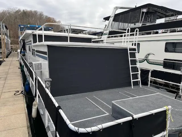 Slide: The Image of 1976 Sumerset 12x55 houseboat docked, featuring a spacious deck and ladder access. - 12