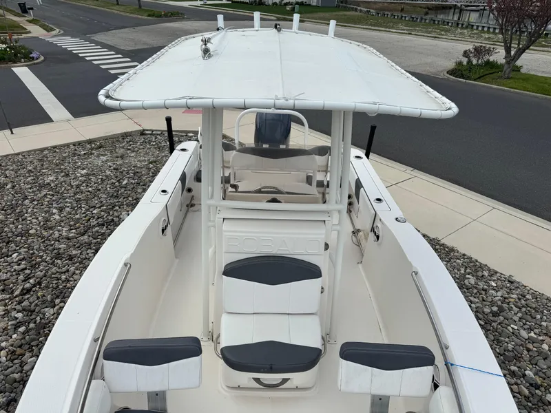 Slide: The Image of 2018 Robalo R200 Center Console boat with white seating and canopy, parked on gravel. - 6