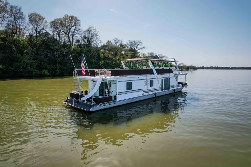 The Image of 1999 Sumerset houseboat on a calm lake, surrounded by trees under a clear blue sky. - 1