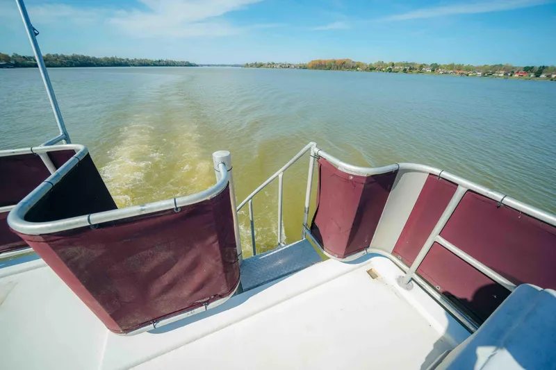 Slide: The Image of 1999 Sumerset houseboat deck with maroon railings, cruising on a calm lake. - 13