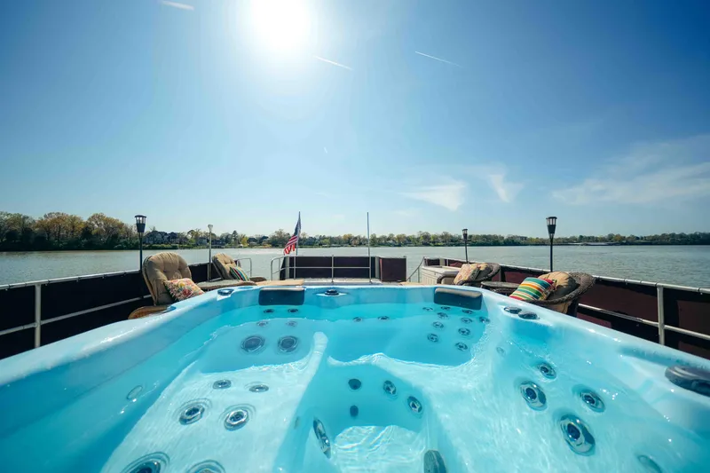 Slide: The Image of Sumerset 1999 houseboat with hot tub on deck, overlooking serene lake under clear blue sky. - 20