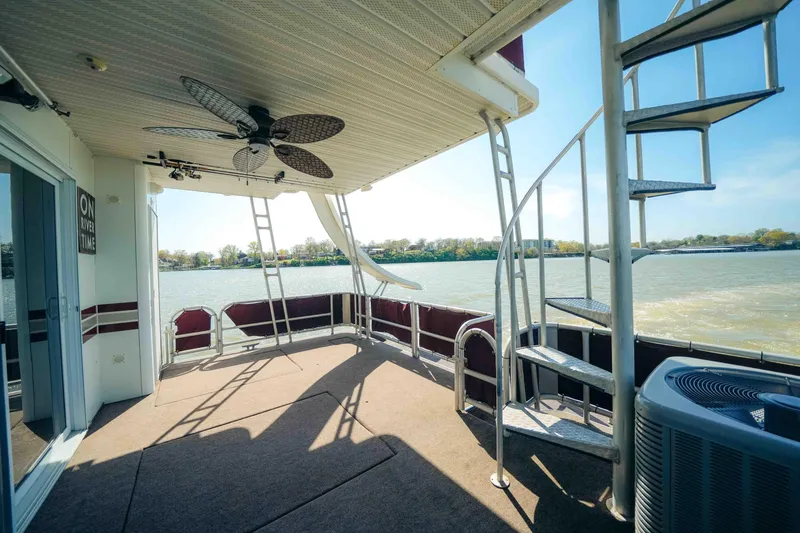 Slide: The Image of 1999 Sumerset houseboat deck with spiral staircase and ceiling fan, overlooking a scenic river view. - 7