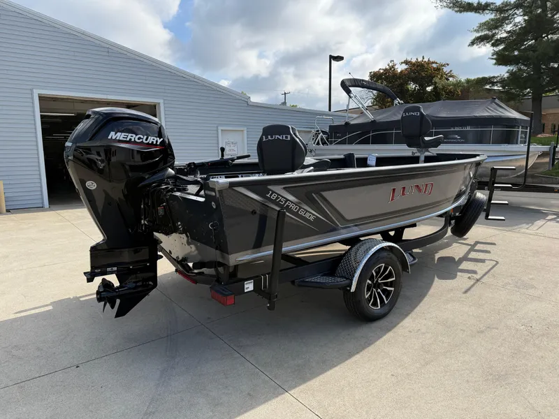Slide: The Image of 2025 Lund 1875 Pro Guide boat with Mercury engine on trailer, parked outdoors. - 5